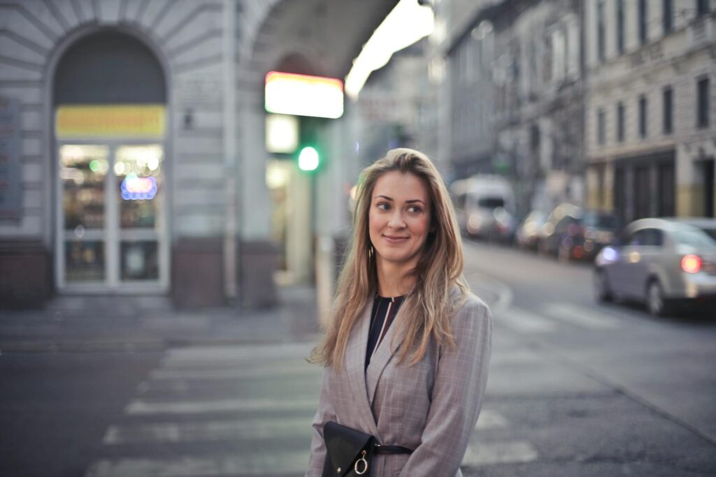 Woman smiling confidently in urban Budapest street scene with vibrant evening lights.